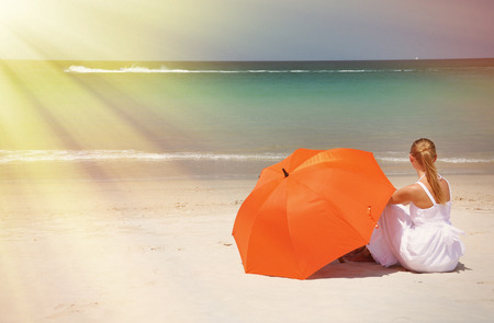 Girl with an orange umbrella on the sandy beachの写真素材