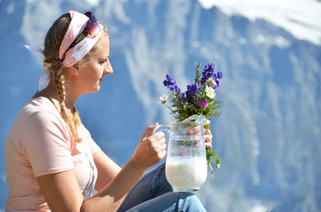 Girl holding a jug of milk and flowers against Swiss Alpsの写真素材