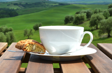 Coffee cup and cantuccini on the wooden table against olive grove. Tuscany, Italyの写真素材