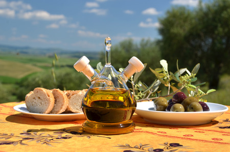 Olive oil, olives and bread on the wooden table against Tuscan landscape. Italyの写真素材