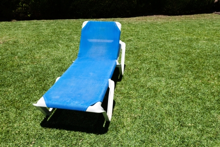 Blue lounger on a manicured green lawn to relax and enjoy the summer vacation reclining in the sunshineの写真素材