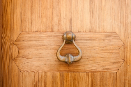 Brass door knocker hanging on a wooden door for gaining access or entry by creating a noiseの写真素材