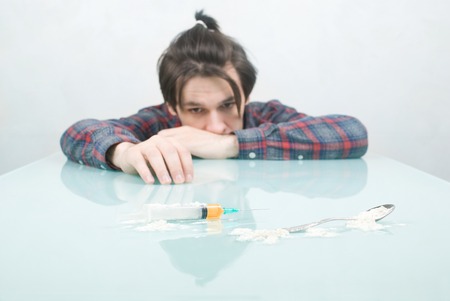 young guy looks at a syringe with heroinの写真素材