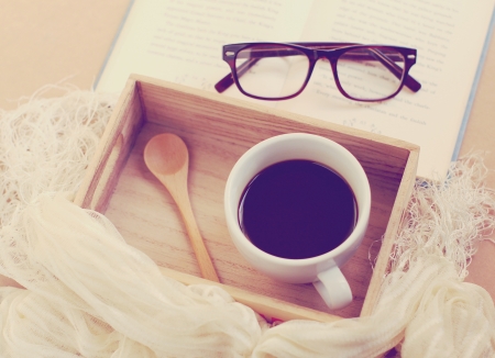 Eyeglasses and book with black coffee on wooden tray, retro filter effectの写真素材
