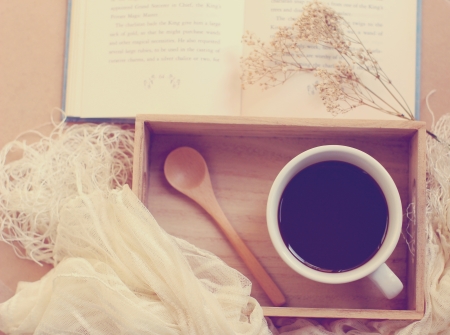 Black coffee and spoon on wooden tray with book, retro filter effectの写真素材