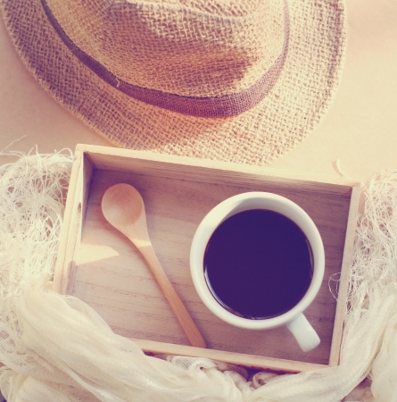 Straw hat with black coffee and spoon on wooden tray, retro filter effectの写真素材