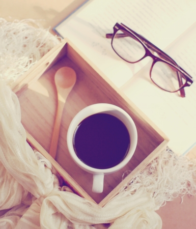 Eyeglasses and book with black coffee on wooden tray, retro filter effectの写真素材