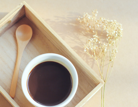 Black coffee and spoon on wooden tray with dried flower, retro filter effectの写真素材
