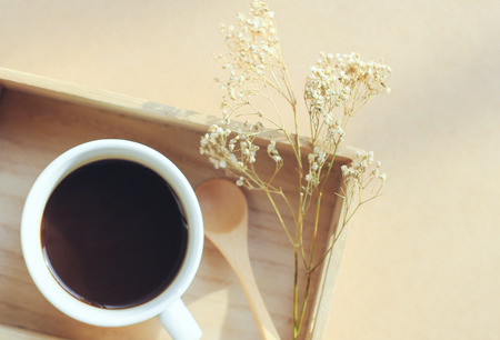 Black coffee and spoon on wooden tray with dried flower, retro filter effectの写真素材