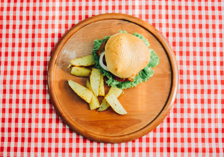 Top view of tasty burger on wooden tray with red tableclothの写真素材