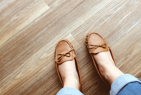 Woman's legs in jeans wearing leather flat shoes on wooden floorの写真素材