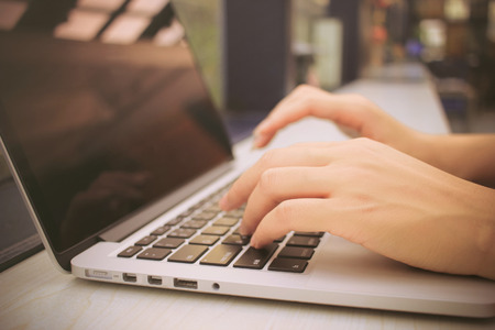 Female hands typing on keyboard of laptop with retro filter effect