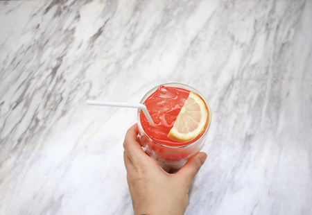 Hand holding iced soft drink on white marble texture table backgroundの写真素材