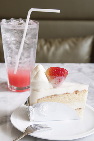 Piece of strawberry cake on white plate with cool drink in the cafeの写真素材