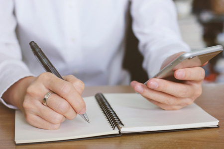 Woman hands using smartphone and writing on notebookの写真素材