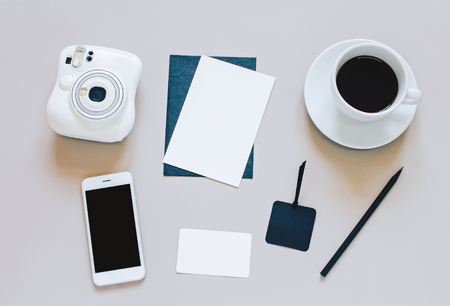 Creative flat lay photo of workspace desk with blank card, coffee, tag, smartphone and camera on grey backgroundの写真素材