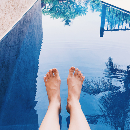 Female legs with red pedicure in the pool water