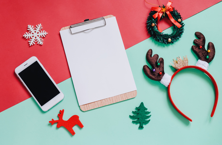 Holiday concept : Flat lay of Christmas ornaments and blank clipboard with smartphone on green and red backgroundの写真素材
