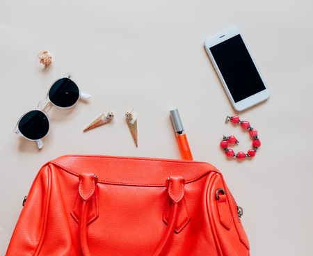 Flat lay of red leather woman bag open out with cosmetics, accessories and smartphone on yellow backgroundの写真素材