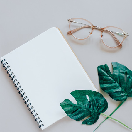 Flat lay of minimal workspace desk with notebook, eyeglasses and green plant, copy spaceの写真素材
