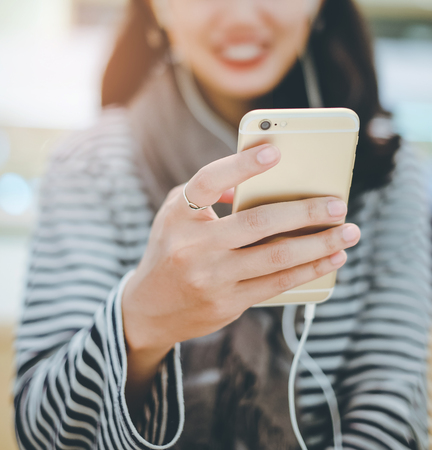 Close up hand of young asian woman playing music with her smartphone and wearing earphones, lifestyle conceptの写真素材