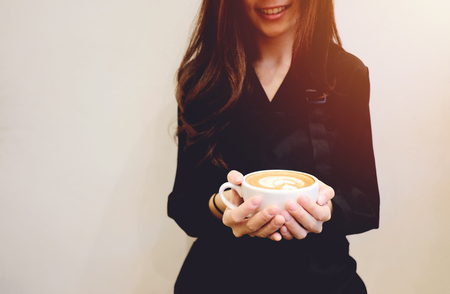 Close up hands of barista woman holding cup of hot cappuccino or latte coffee and smiling in the cafe, copy spaceの写真素材