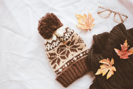 Flat lay of autumn fashion style, scarf, knitted hat and eyeglasses with maple leaves on white sheet backgroundの写真素材