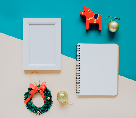 Creative flat lay of craft and photo frame, blank notebook mock up with christmas ornaments and gift box on colorful background, minimal styleの写真素材