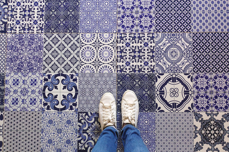 Selfie of feet with sneaker shoes on art pattern tiles floor background, top view