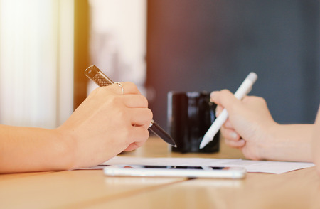 Close up of two businesswomen hands signing a document in workplace with sunlight filter  の写真素材