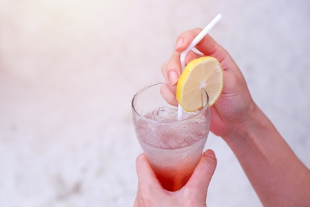 Woman hands holding glass of iced summer drink with lemon sliced at sand beachの写真素材