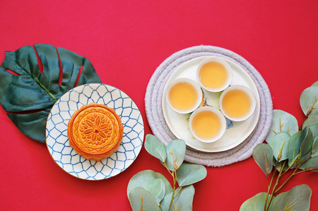 Flat lay of chinese moon cake with hot tea and green plant on red background, holiday and festival conceptの写真素材