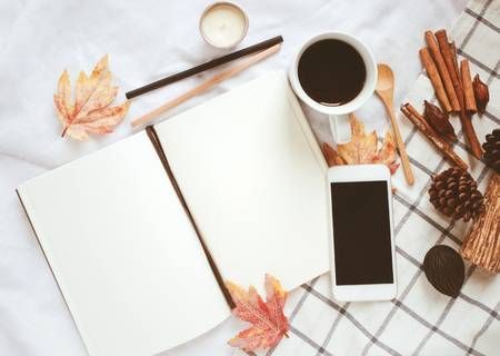Autumn lifestyle concept, blank notebook, smartphone and coffee with autumn leaves ornaments on white bed sheet backgroundの写真素材