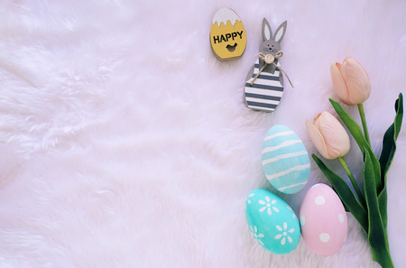 Happy Easter concept with wooden bunny and colorful easter eggs on white fur background and pink tulips. Top view with copy spaceの写真素材