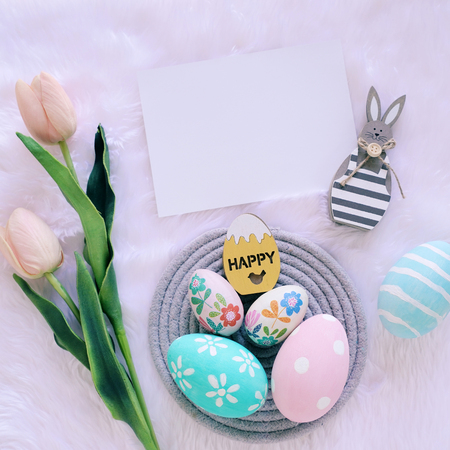 Happy Easter concept with wooden bunny and colorful easter eggs on white fur background and pink tulips. Top viewの写真素材