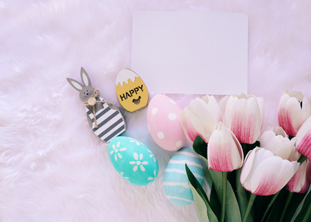 Happy Easter concept with wooden bunny and colorful easter eggs on white fur background and pink...