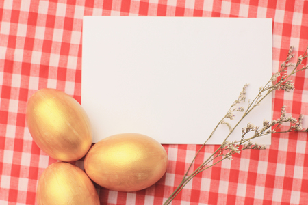 Golden easter eggs on red checkered tablecloth background with blang greeting card, happy easter holidayの写真素材