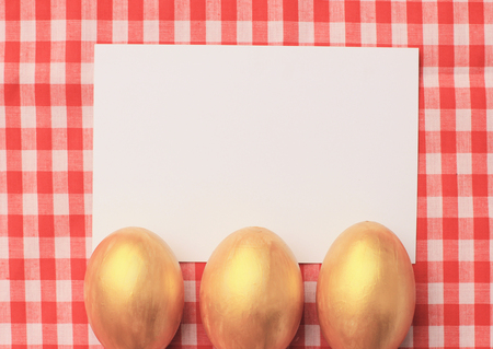 Golden easter eggs on red checkered tablecloth background with blang greeting card, happy easter holidayの写真素材