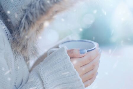 Close up woman hands holding hot cup of coffee or tea in cold snow background, wearing warm fur knitted clothesの写真素材