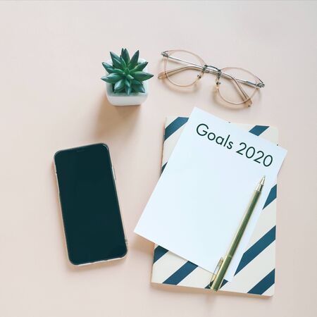 Goals 2020 on flat lay photo of workspace desk with smartphone, card and notebook with copy space background, minimal style and mockup conceptの写真素材