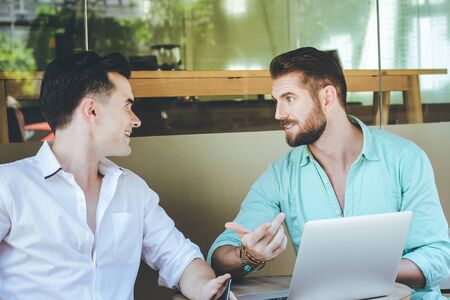 Two young caucasian businessmen meeting and brainstorming while using laptop at outdoor cafe, business and lifestyle conceptの写真素材
