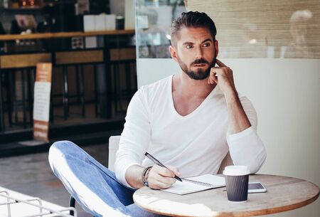 Smart young hipster businessman thinking while writing on notebook at sidewalk cafe, lifestyle and...