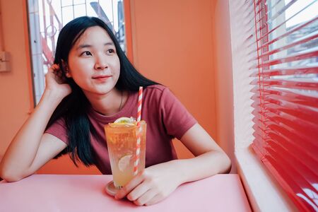 Young asian millennial woman drinking tasty lemonade in the pastel cafe, summer and lifestyle conceptの写真素材