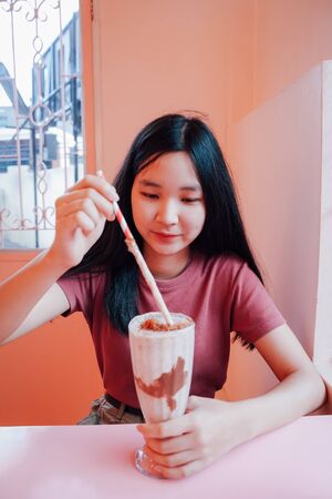 Young asian millennial woman drinking tasty milkshake in the pastel cafe, summer and lifestyle conceptの写真素材