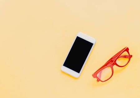 Flat lay of lifestyle items with smartphone and red eyeglasses on bright yellow background, fashion style summer の写真素材
