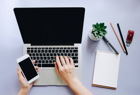 Flat lay of workspace desk with woman hands typing on laptop and using smartphone with note paper...