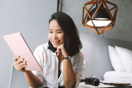 Portrait of attractive asian woman making facetime video calling or meeting online with tablet at her home, working remotely and social distancing, self quarantine conceptの写真素材
