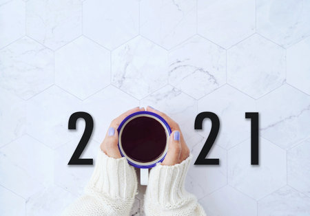 Start to new year 2021 concept ,top view of woman hands holding hot cup of coffee on white marble background, goals and plans for motivationalの写真素材