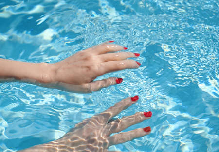 Close up of woman hands with manicure in red under clear pool water background, fashion and sport conceptの写真素材