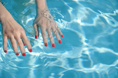 Close up of woman hands with manicure in red under clear pool water background, fashion and sport conceptの写真素材
